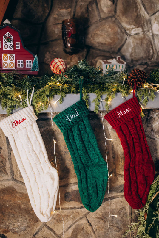 Three Christmas stockings labeled 'Ethan', 'Dad', and 'Mom' hanging on a fireplace mantle with decorative items.