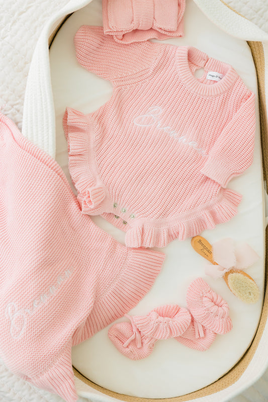 Pink baby outfit with ruffled details on a white surface