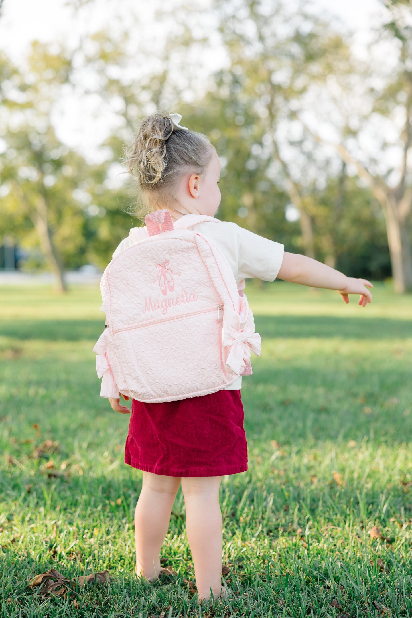 Child wearing a pink backpack in a park