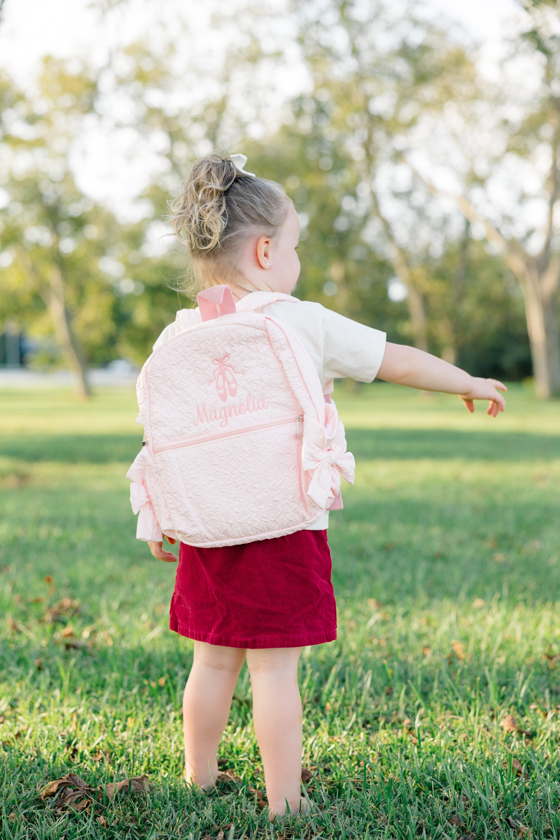 Child wearing a pink backpack in a park