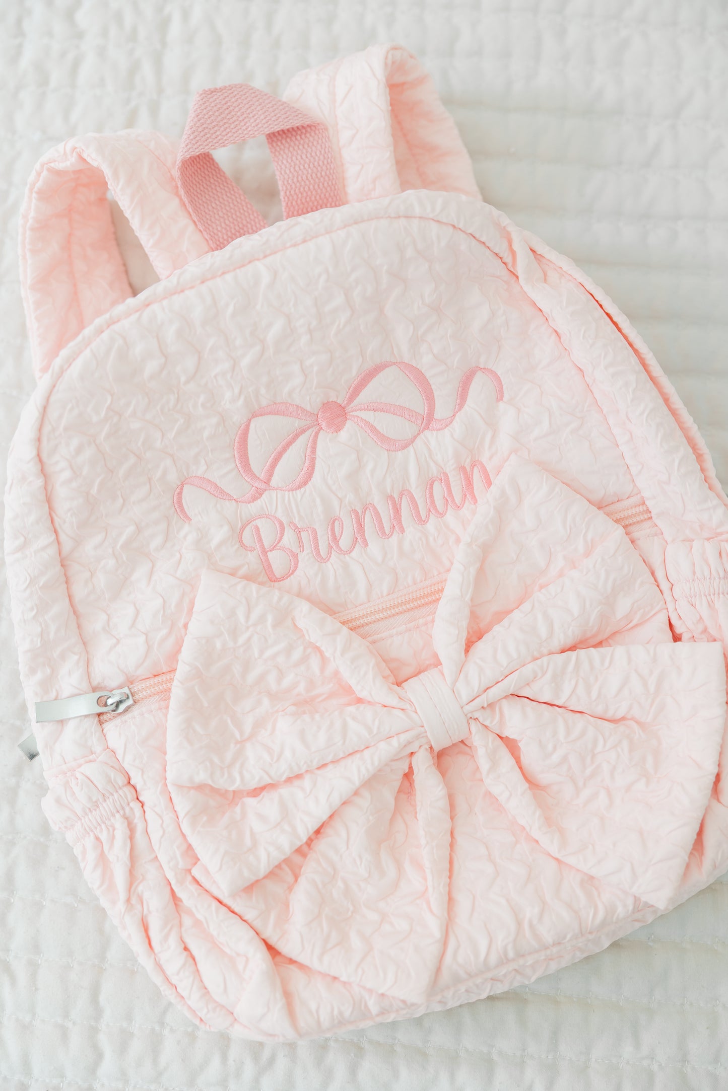 Pink textured backpack with bow design and embroidered name on a light background