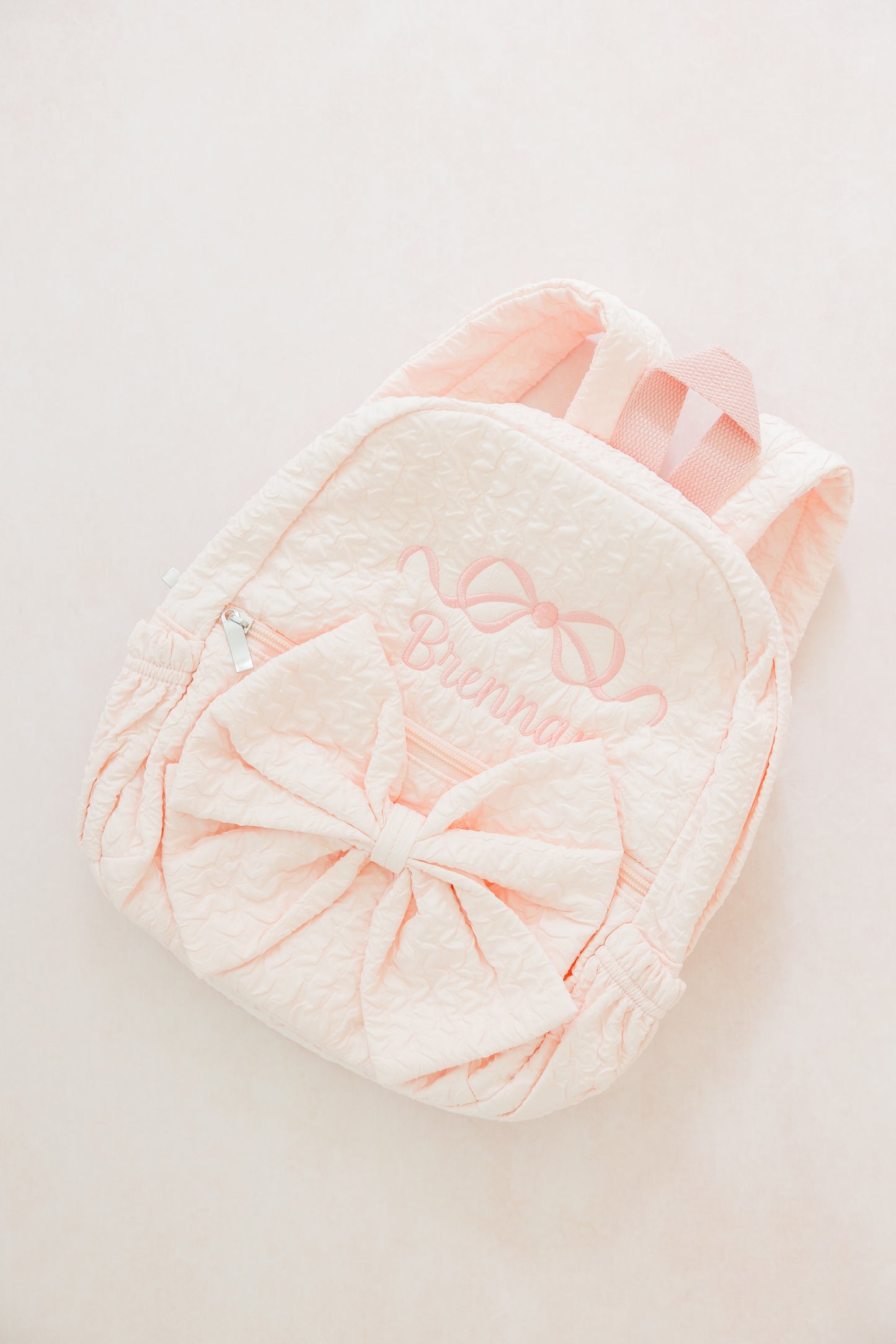 Pink plush backpack with decorative bow on a light gray background