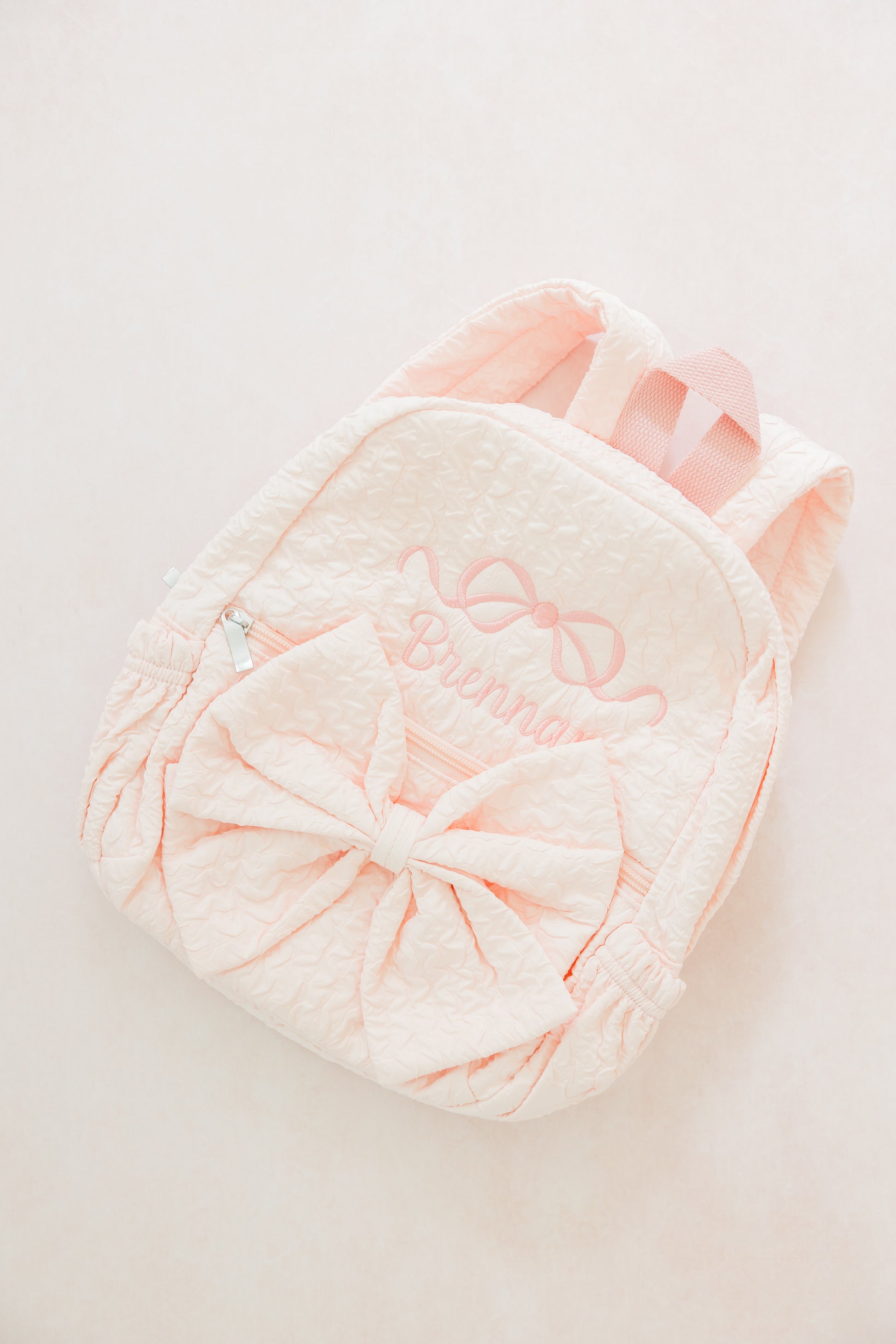 Pink plush backpack with decorative bow on a light gray background