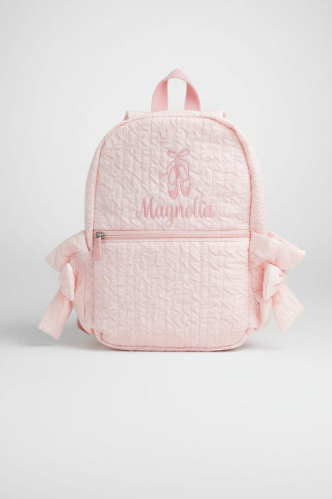 Child in pink outfit with backpack walking outdoors on grass