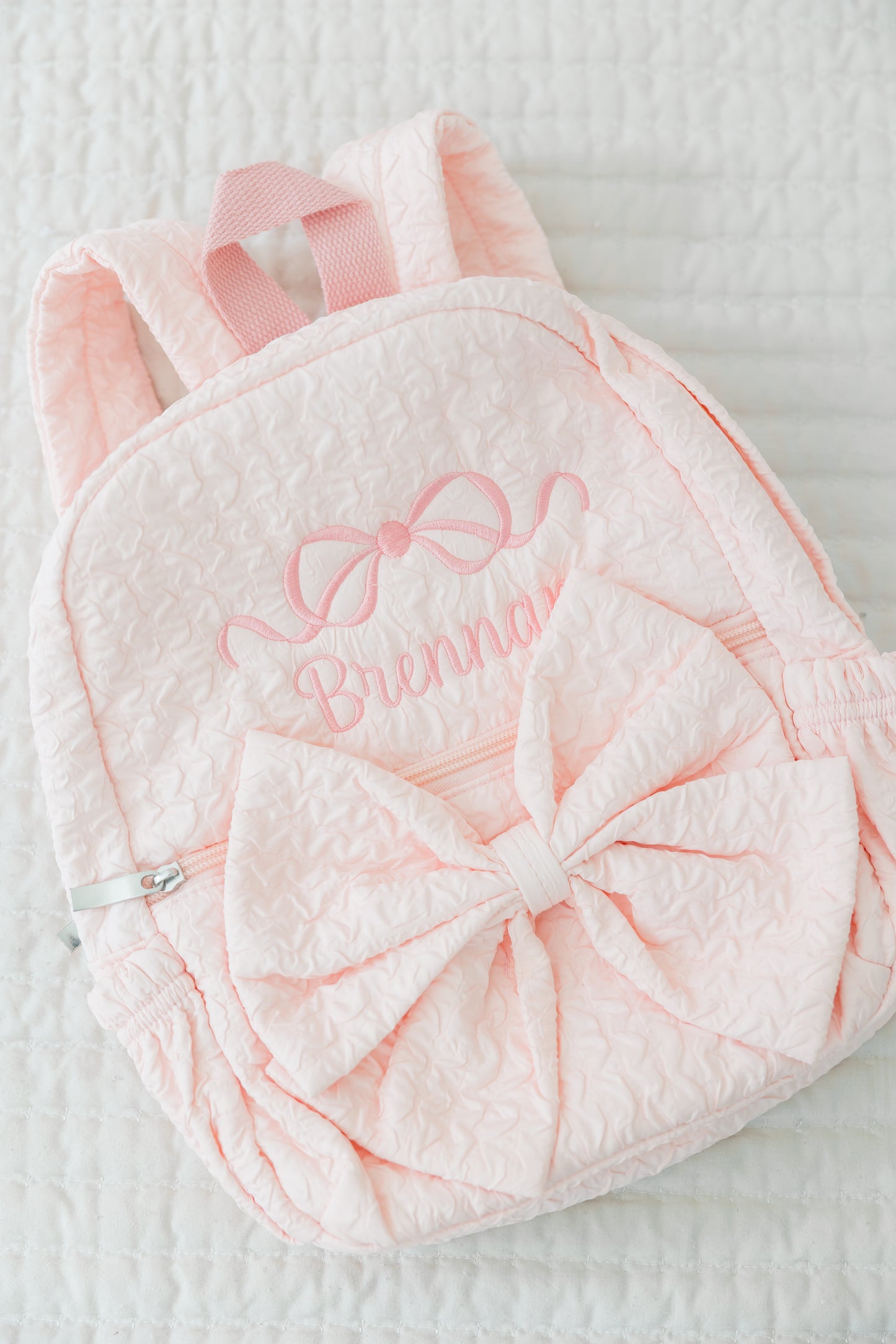 Pink backpack with bow and embroidered name on a textured surface