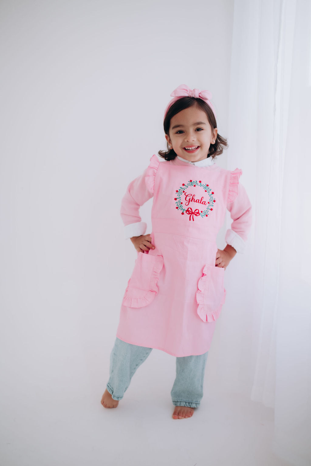 Child wearing a pink apron with floral design and text on a white background
