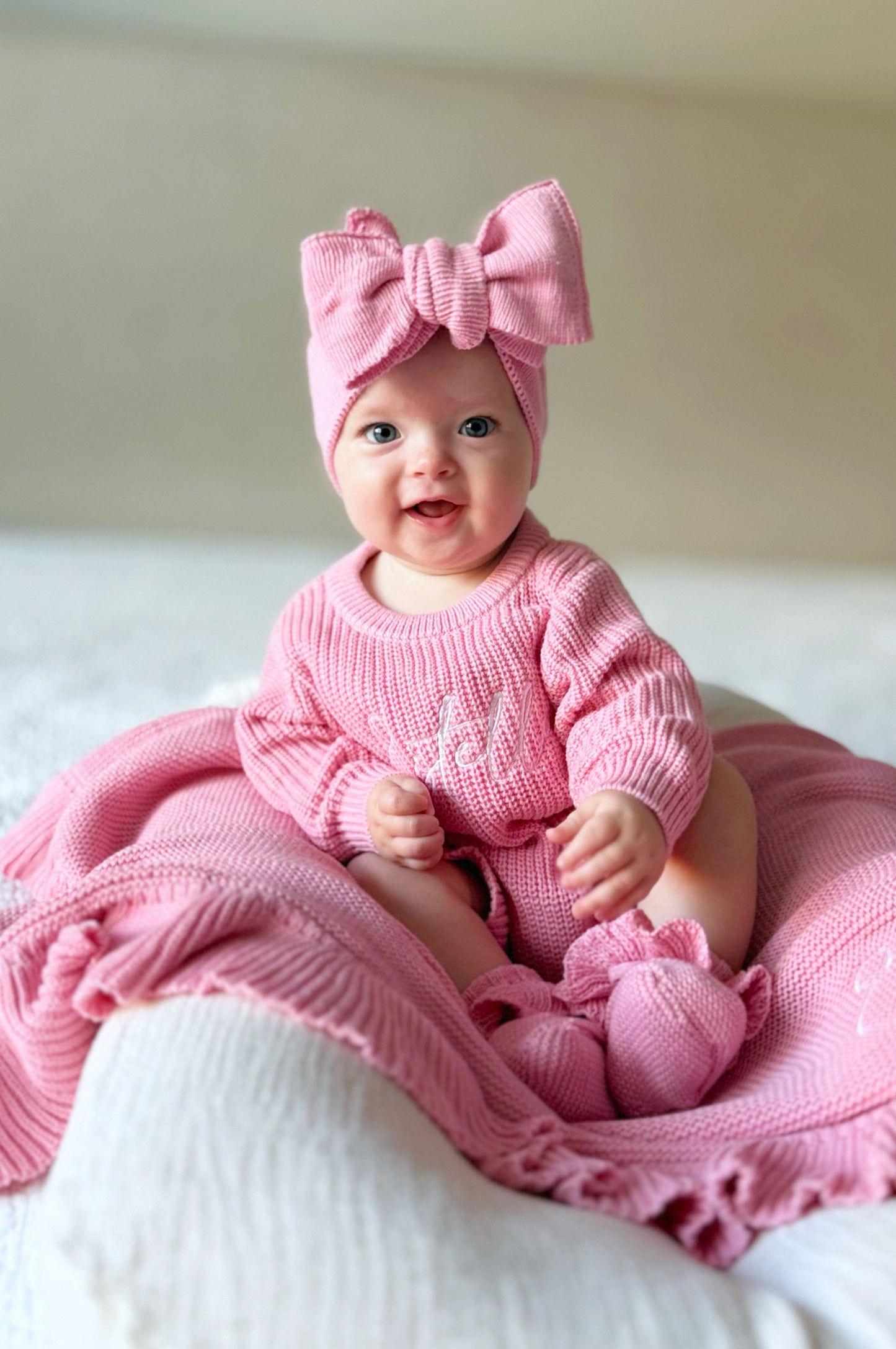 Baby in pink outfit with a large bow sitting on a pink blanket.