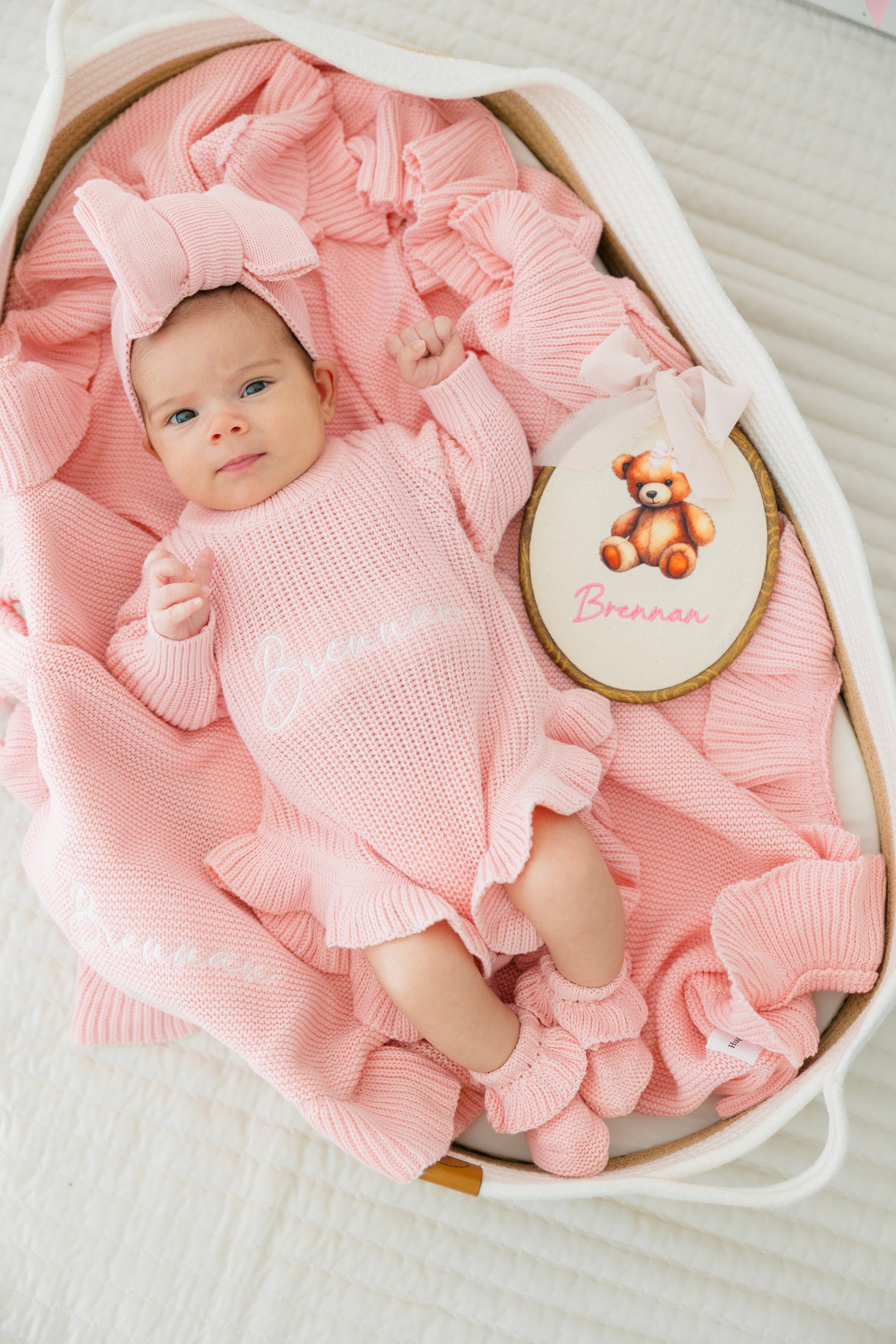 Baby in pink outfit with bow and teddy bear emblem in a basket