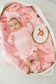Baby in pink outfit with bow and teddy bear emblem in a basket
