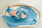Newborn baby in blue outfit and hat lying on a blue blanket with 'Asher' embroidered, in a white basket.