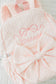 Pink textured bag with bow and embroidered name on a light background