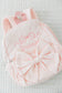 Pink backpack with bow and embroidered name on a textured surface